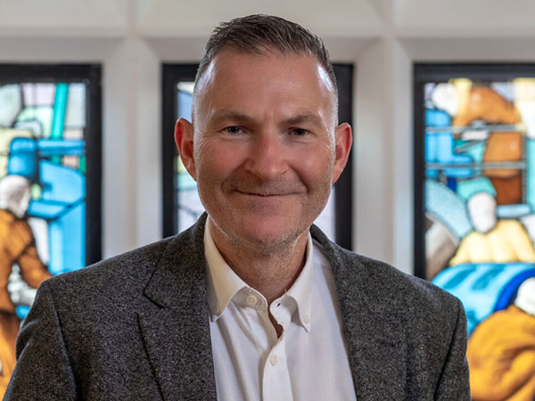Portrait of John Downey against a stained glass window.