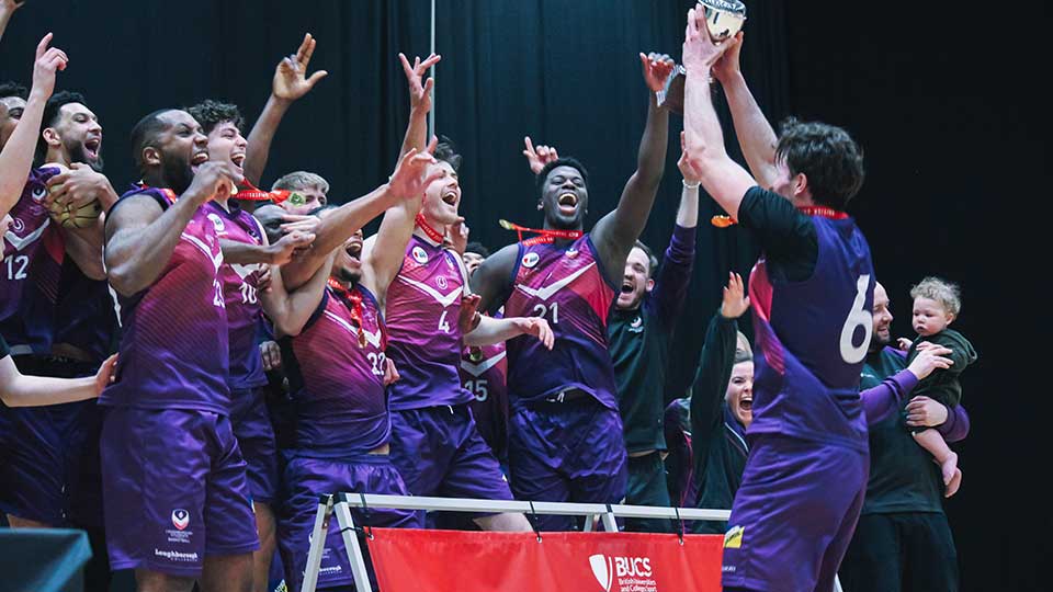 Students lifting a trophy, celebrating, wearing Loughborough Sport kit