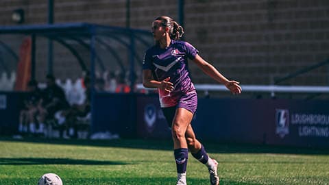 A Lightning player is dribbling a football at her feet on the football pitch.