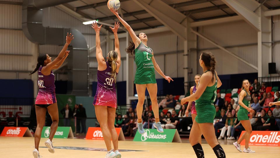 A netball match in progress with one player mid air catching the ball
