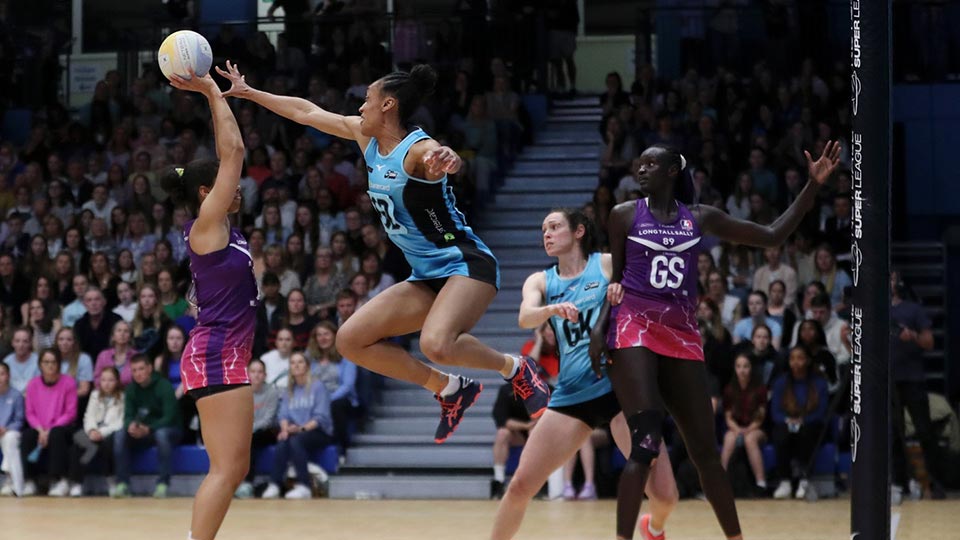 A netball match in progress with one player jumping to reach the ball