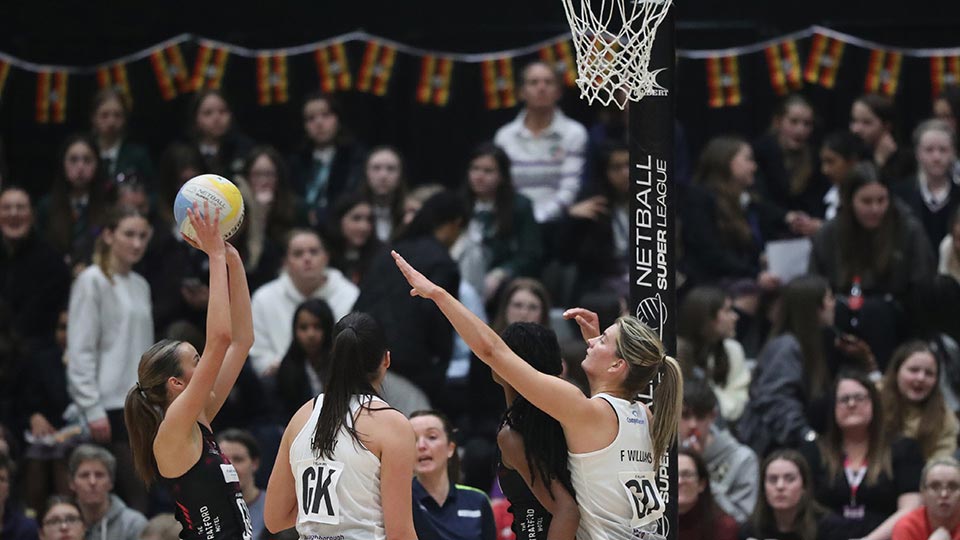 A netball player about to take a shot while other players are trying to defend