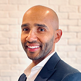 A headshot photo of Mark Simpson smiling, wearing a suit