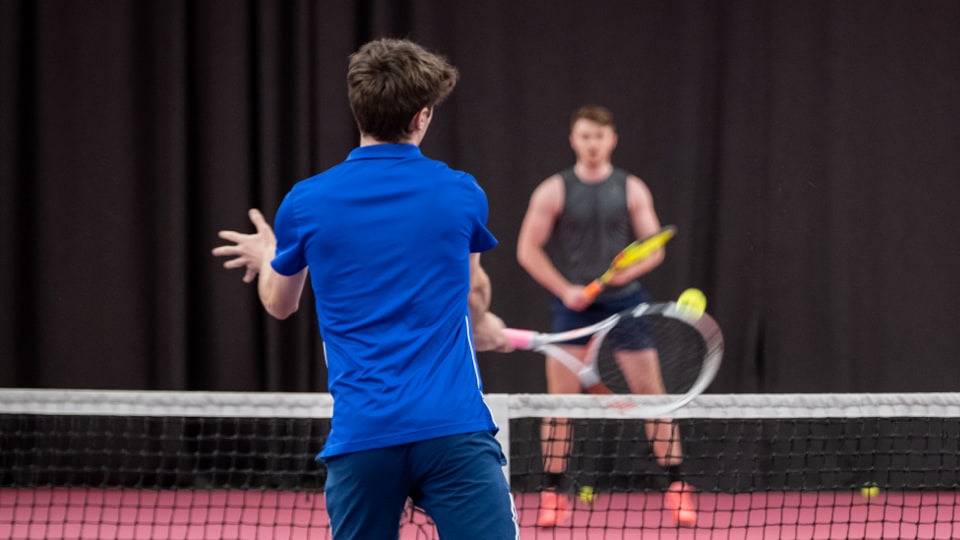 Two men playing tennis on an indoor court