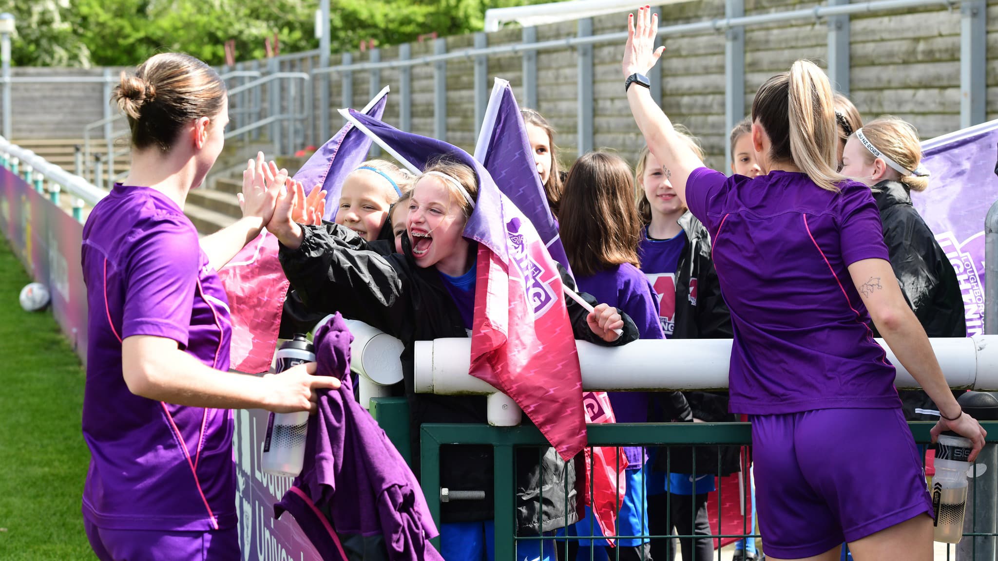 Two Loughborough Lightning FC players interacting with spectators who are smiling and laughing