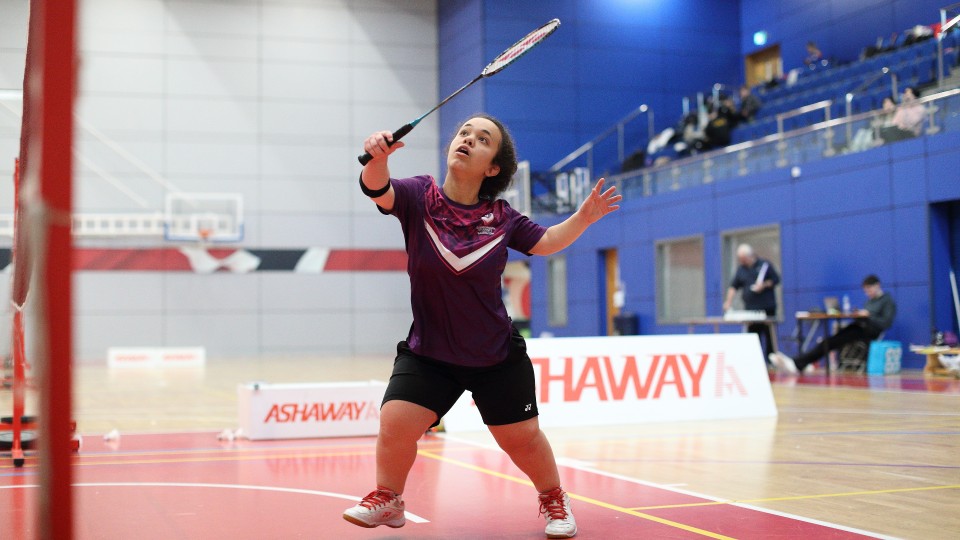 A badminton player on the court holding their racket in the air and about to return the shuttlecock