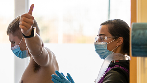 a man with his arms raised and a physiotherapist standing behind looking at his back