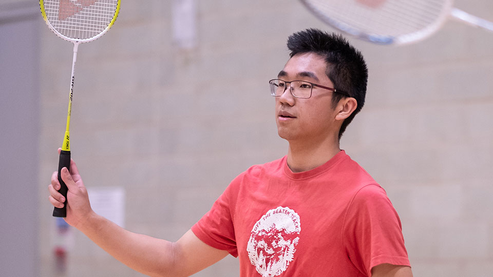 Man with glasses holding yellow badminton racket during a badminton match