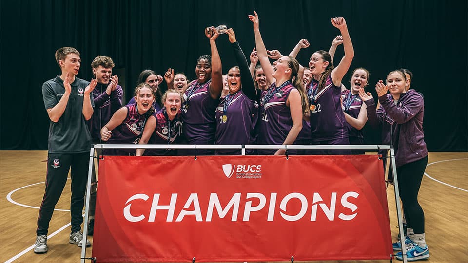 a basketball team celebrating and cheering, they are standing behind a red banner which says 'championship'