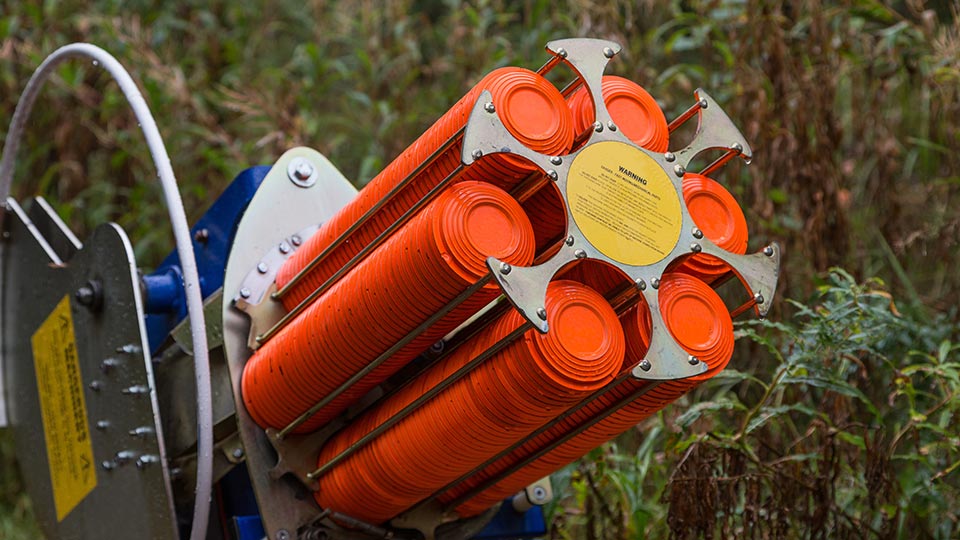 A machine featuring orange and yellow barrels stacked on top for clay pigeon shooting