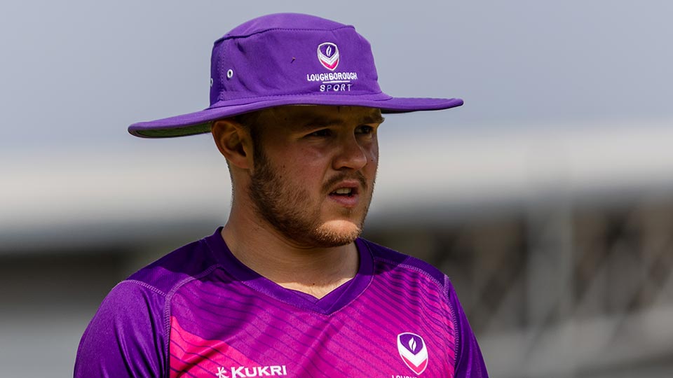 A cricketer in a vibrant purple and pink uniform wearing a purple hat