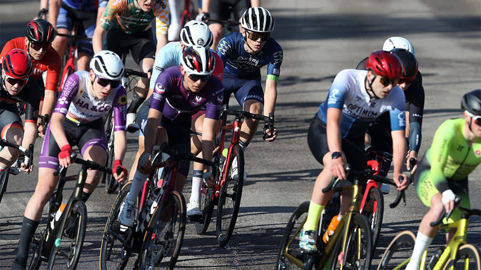 The photo captures a cycling race in action. There are around 10 cyclists visible on the photo, wearing cycling gear.