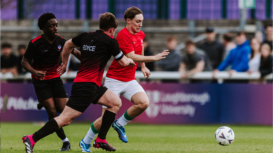 A Loughborough Men's Football player breaking with the ball as opposing players chase to defend