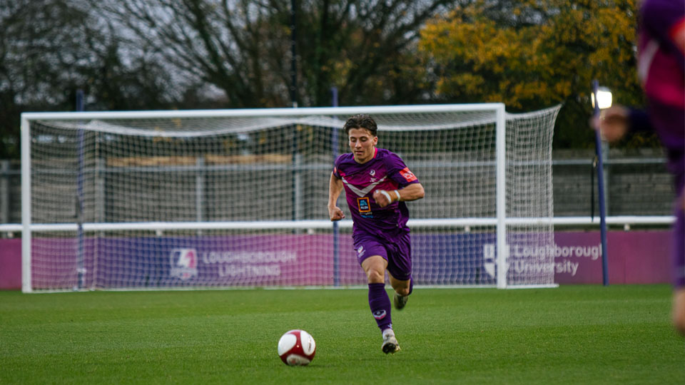 A Loughborough Men's football player running with the ball at his feet, towards the opposing goal