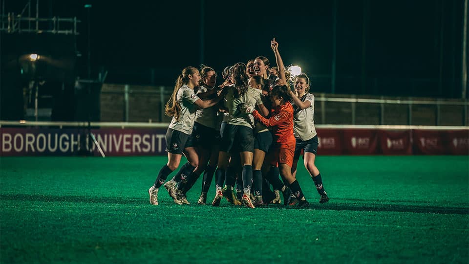 the female team cheering and celebrating on the pitch, gathered in the circle.