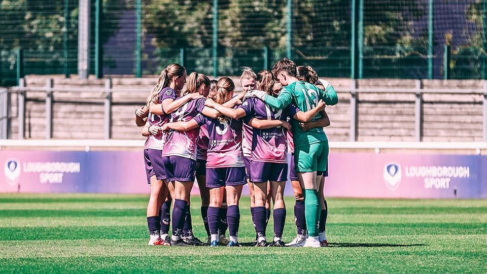 The Loughborough Lightning football team standing in a huddle on the pitch.