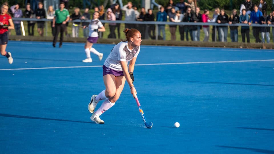 a hockey player on a blue pitch about to hit the ball