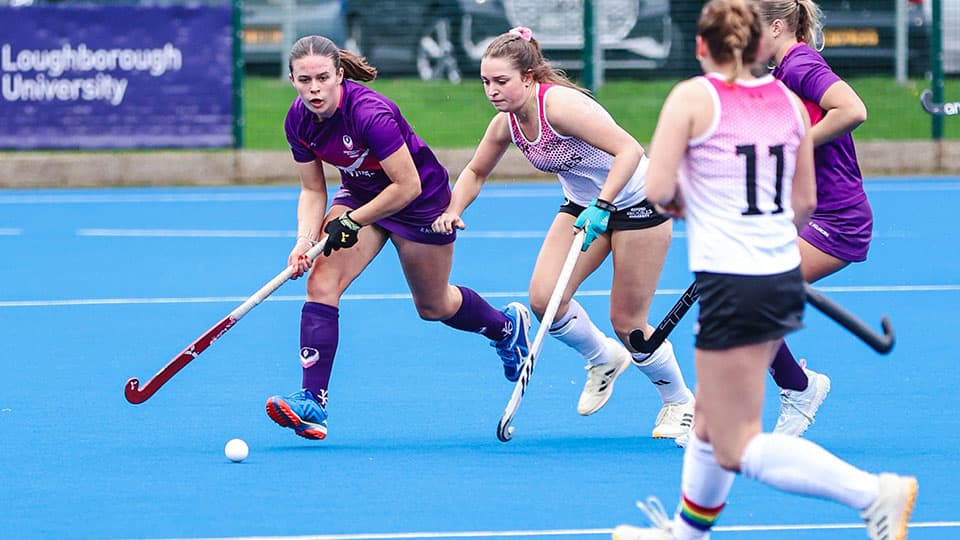players chasing the ball on a blue hockey pitch