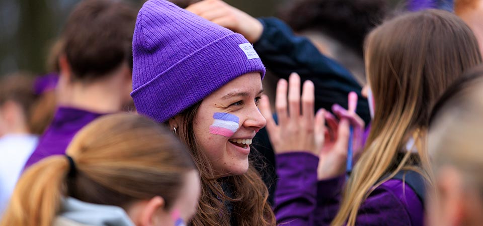A person wearing a purple hat smiling in a crowd