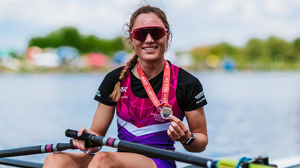 A female rower wearing Loughborough kit sat in their boat holding up a medal