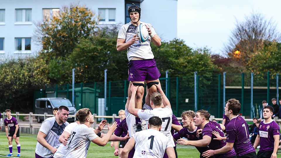 Men's ruby union match in progress with one player being held up in the air holding the ball