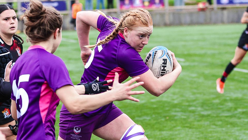 A women's rugby union match in progress and one player is running with the ball