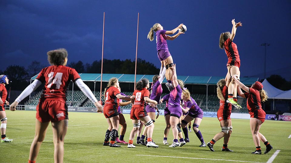 A women's rugby union match in progress and one player is being lifted in the air holding the ball