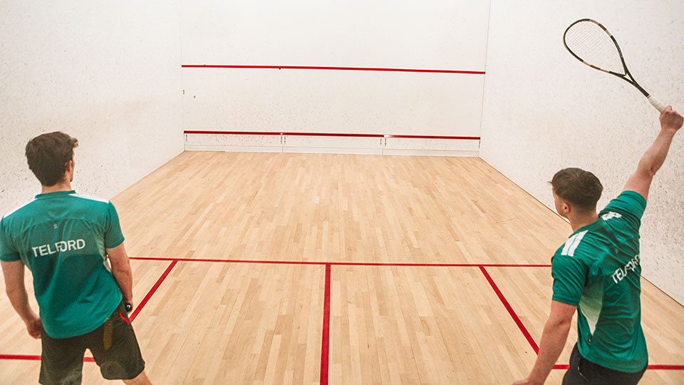 Two squash players wearing green Telford t-shirts playing a match