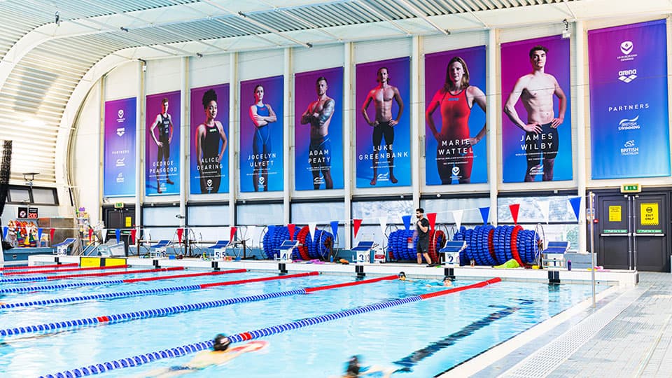 the swimming pool with people swimming in lanes and large banner images on the end wall