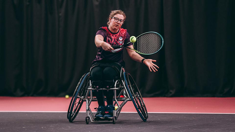 A wheelchair tennis player about to hit the ball with their racket