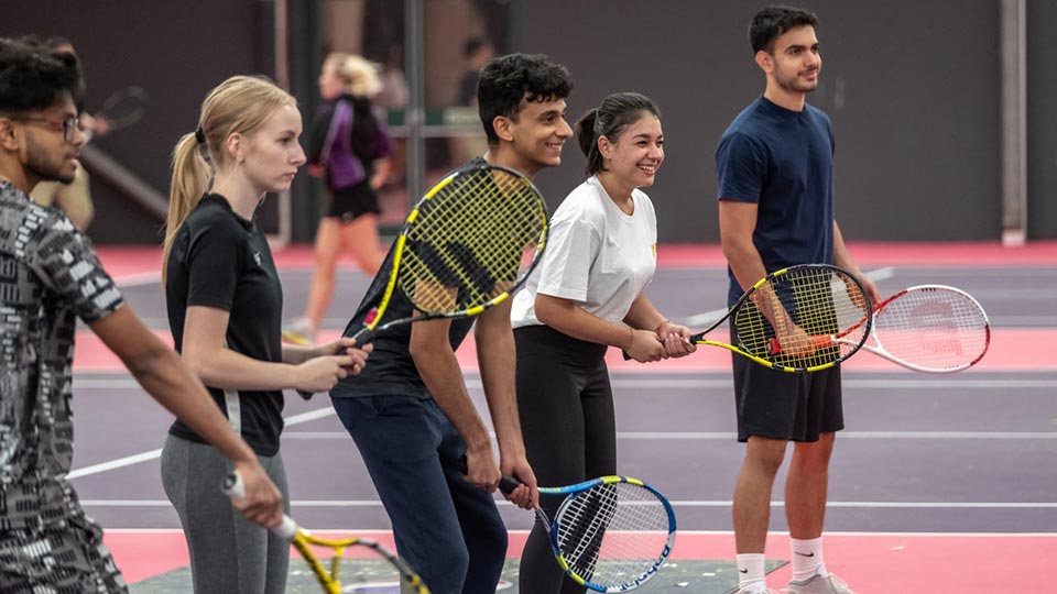 A group of students stood in a row holding tennis rackets