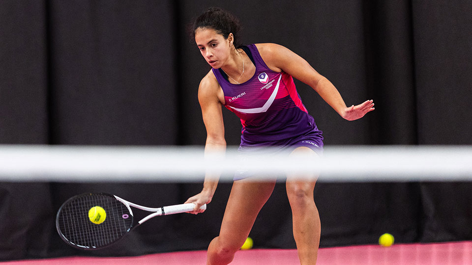 An action shot of a female tennis player holding a racket and about to hit the ball