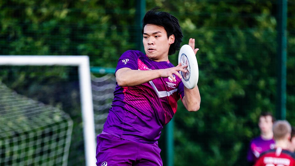 An ultimate frisbee player on the pitch, one holding the frisbee
