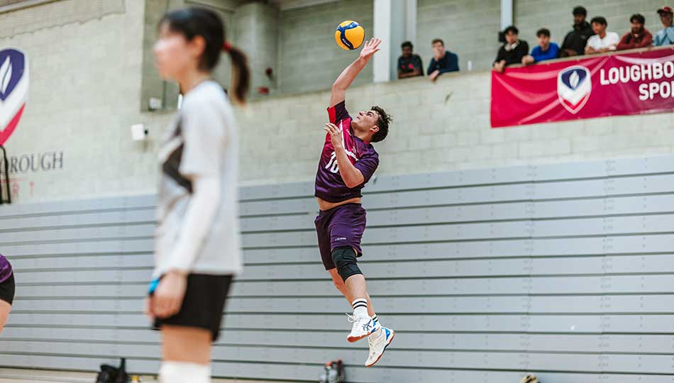 A volleyball player wearing purple Loughborough kit reaching up high to hit a ball