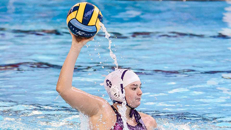 The water polo player in the pool holding the ball above their head