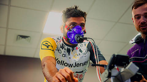 A triathlete has a mask on while riding a bike in a lab.