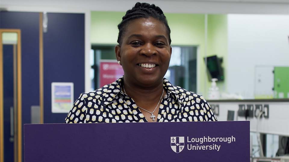 Sheryl holding a large piece of purple card with the University logo printed on it
