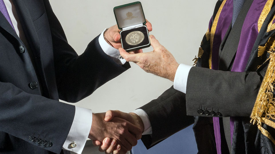 Closeup of senior academic shaking hands with student in business attire, whilst handing over the Sir Robert Martin medal.