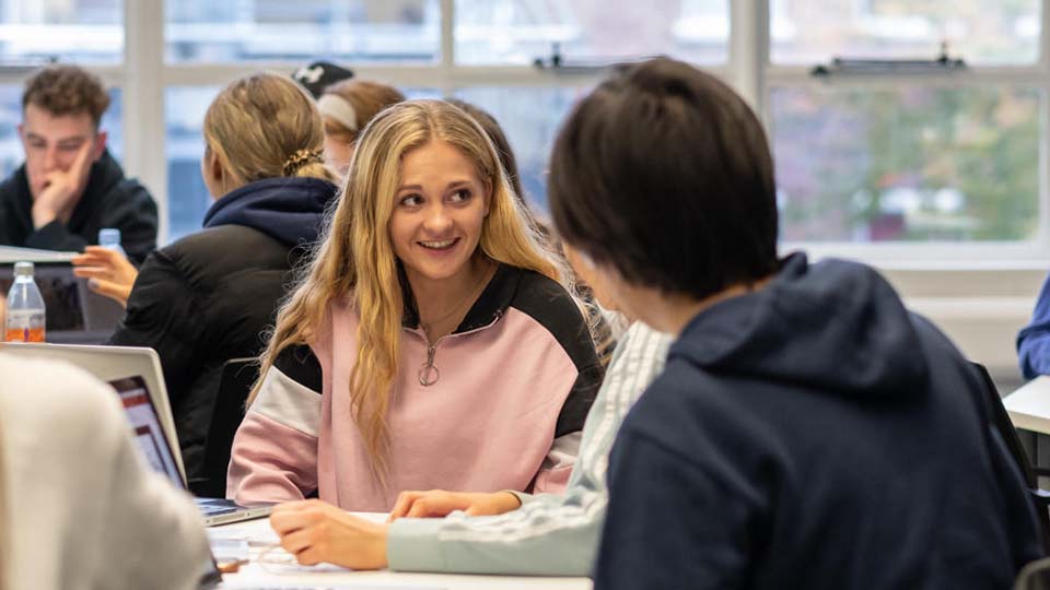 Girl in pink top in lecture with others, looking excited but nervous