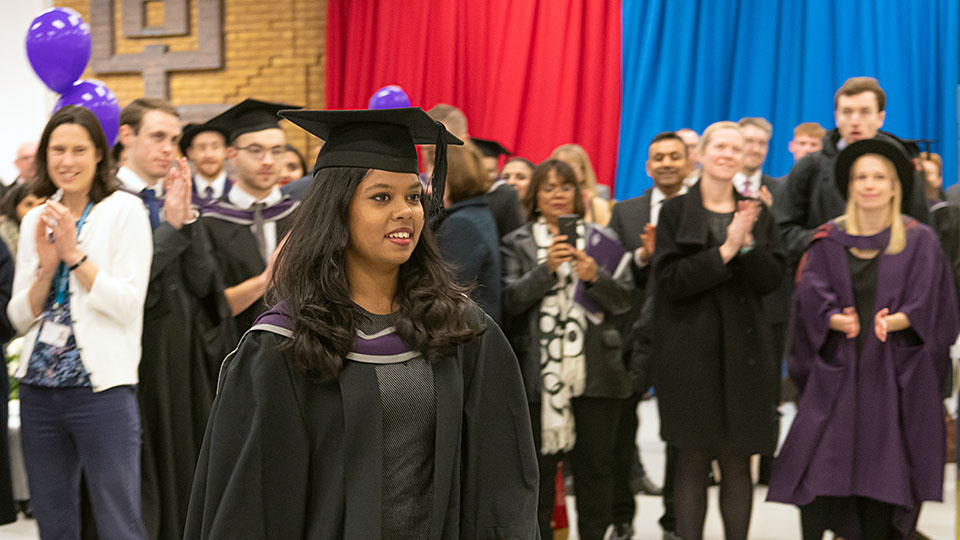 Sports student in graduation gown, going up to receive her School prize, with everyone in the background applauding (and artfully out of focus).
