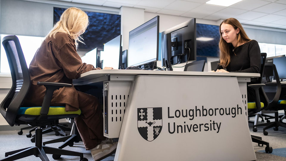 Two students working on computers in a University study space.