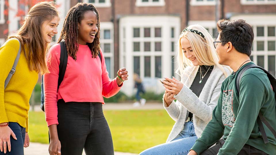 A small group of cheerful, chatting students by the fountain outside Hazlerigg, with one inevitably on their phone.