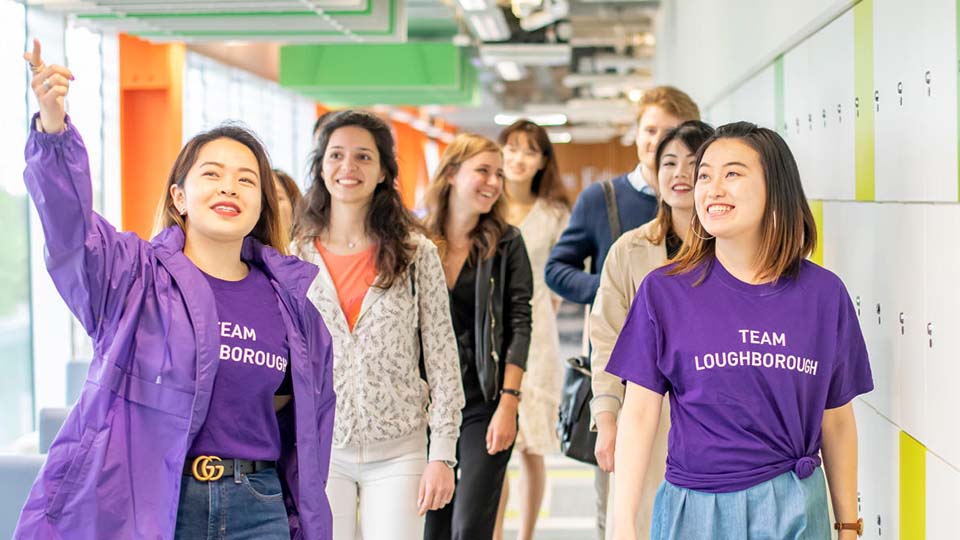 Two smiling students wearing Team Loughborough t-shirts giving prospective students a tour of campus.