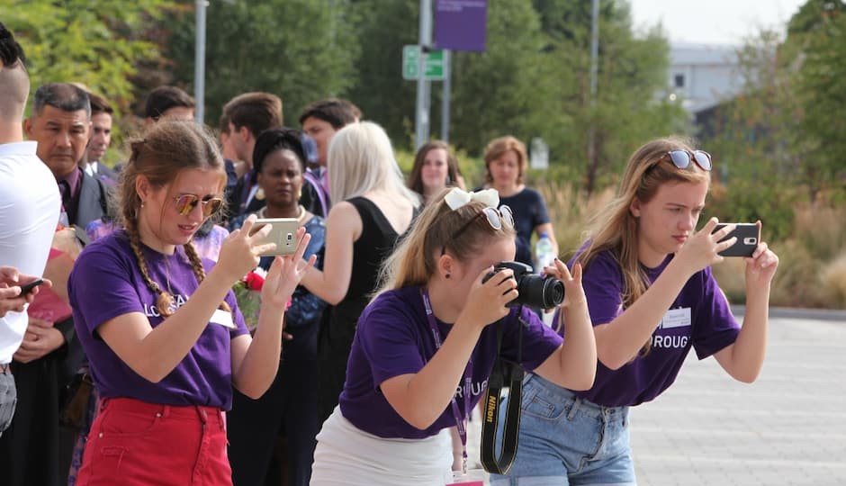 Three student ambassadors, wearing purple T-shirts, taking photos with their mobile phones and a camera.