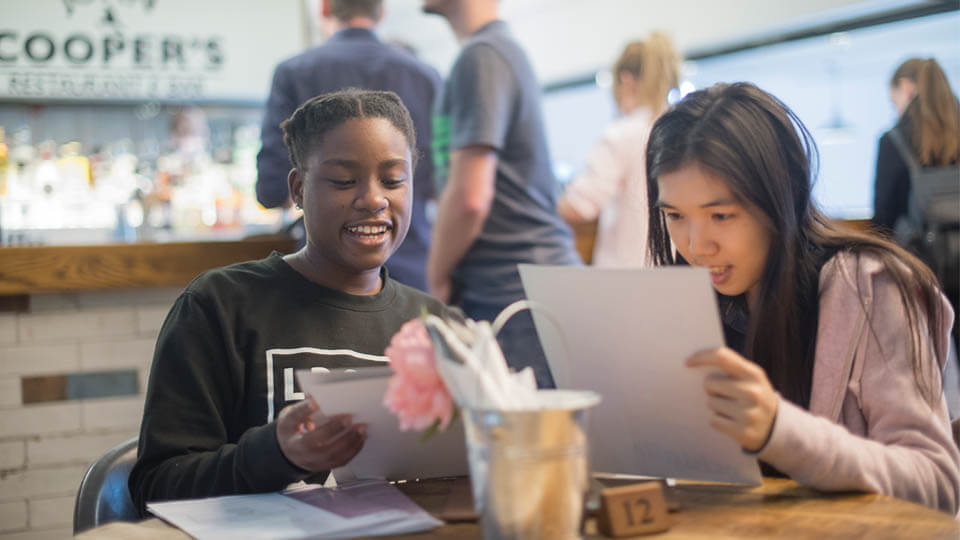 two students enjoying a drink and looking at a menu in John Coopers