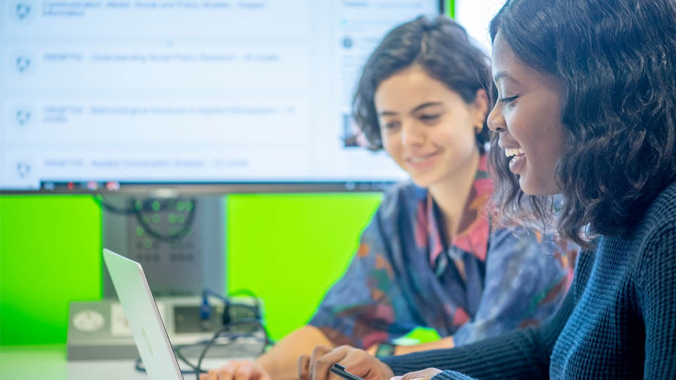 learn on screen behind two students looking at a laptop screen