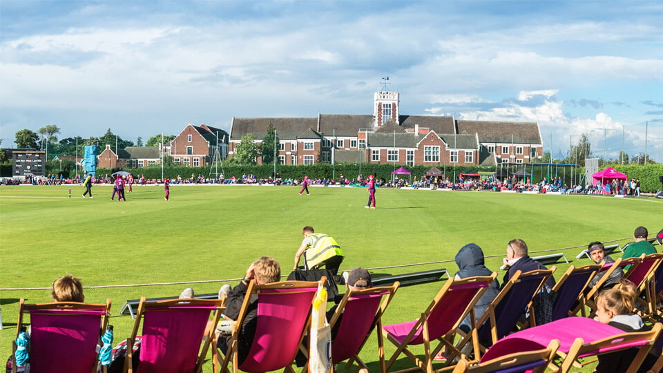 Cricket match in action and spectators sat watching.