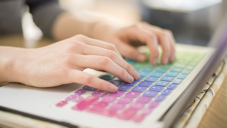 Someone typing on a colourful keyboard.