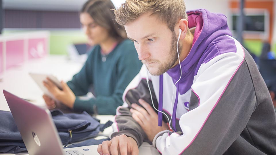 A student sat using their laptop with their headphones on.