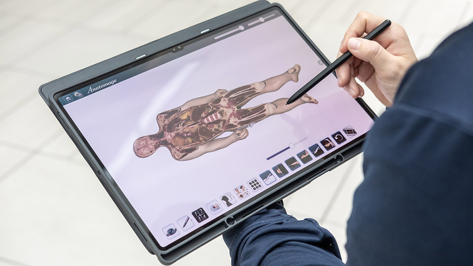 A person holding the Anatomage tablet which shows a 3D anatomy system.